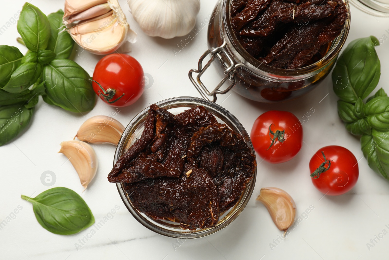 Delicious sun dried tomatoes, fresh vegetables, basil and garlic on white table, flat lay Photo of Delicious sun dried tomatoes, fresh vegetables, basil and garlic on white table, flat lay