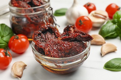 Photo of Delicious sun dried tomatoes, fresh vegetables, basil and garlic on white table, closeup
