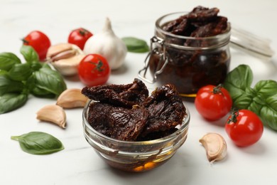 Photo of Delicious sun dried tomatoes, fresh vegetables, basil and garlic on white table, closeup
