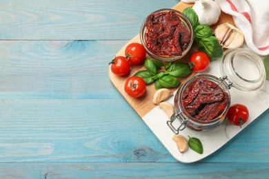 Photo of Delicious sun dried tomatoes, fresh vegetables, basil and garlic on blue wooden table, top view. Space for text