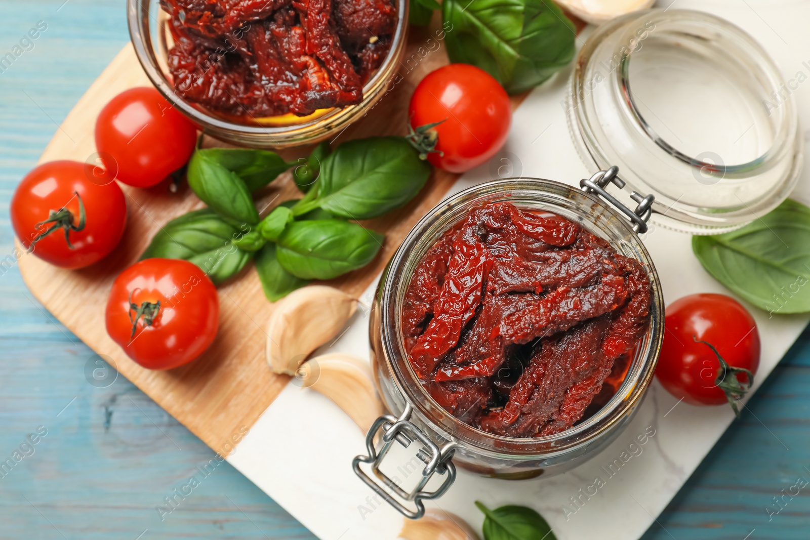 Delicious sun dried tomatoes, fresh vegetables, basil and garlic on blue wooden table, top view Photo of Delicious sun dried tomatoes, fresh vegetables, basil and garlic on blue wooden table, top view