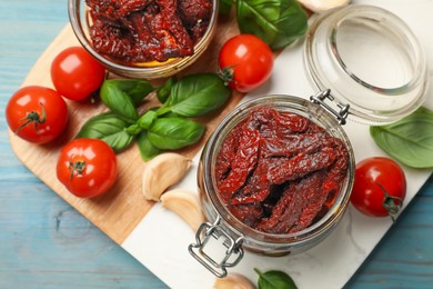 Photo of Delicious sun dried tomatoes, fresh vegetables, basil and garlic on blue wooden table, top view