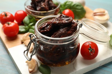 Photo of Delicious sun dried tomatoes, fresh vegetables, basil and garlic on blue wooden table, closeup
