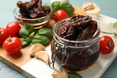 Photo of Delicious sun dried tomatoes, fresh vegetables, basil and garlic on blue wooden table, closeup
