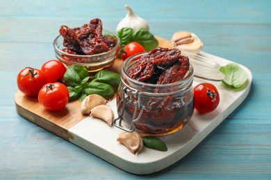 Photo of Delicious sun dried tomatoes, fresh vegetables, basil and garlic on blue wooden table, closeup