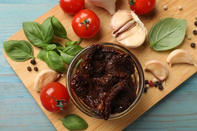 Photo of Delicious sun dried tomatoes, fresh vegetables, basil and garlic on blue wooden table, top view