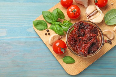 Photo of Delicious sun dried tomatoes, fresh vegetables, basil and garlic on blue wooden table, top view. Space for text