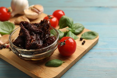 Photo of Delicious sun dried tomatoes, fresh vegetables, basil and garlic on blue wooden table, closeup