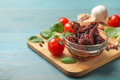 Photo of Delicious sun dried tomatoes, fresh vegetables, basil and garlic on blue wooden table, closeup. Space for text