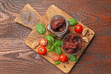 Photo of Delicious sun dried tomatoes, fresh vegetables, basil and garlic on wooden table, top view