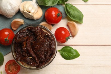 Photo of Delicious sun dried tomatoes, fresh vegetables, basil and garlic on white wooden table, flat lay