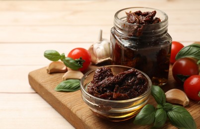 Photo of Delicious sun dried tomatoes, fresh vegetables, basil and garlic on white wooden table, closeup. Space for text