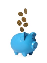 Image of Coins falling into light blue piggy bank on white background