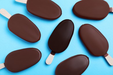 Image of Individuality, uniqueness, different. Ice cream coated in dark chocolate glaze among others coated with milk chocolate on light blue background, flat lay