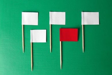 Image of Individuality, uniqueness, different. Red small flag among white ones on green background, flat lay