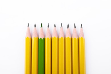 Image of Individuality, uniqueness, different. Green pencil among yellow ones on white background, top view