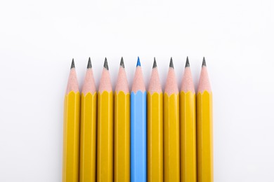 Image of Individuality, uniqueness, different. Light blue pencil among yellow ones on white background, top view