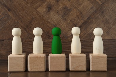 Image of Individuality, uniqueness, different. Green human figure among colorless ones on cubes against wooden background