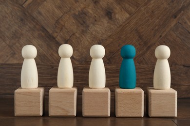 Image of Individuality, uniqueness, different. Blue human figure among colorless ones on cubes against wooden background