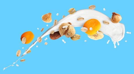 Image of Milk splash with oat flakes and dried fruits on light blue background. Banner design