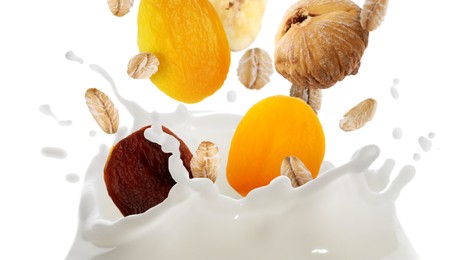 Image of Milk splash with oat flakes and dried fruits in air on white background. Healthy breakfast
