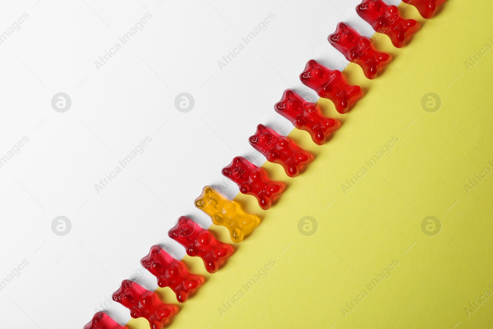 Image of Individuality, uniqueness, different. Orange jelly bear among red ones on color background, top view