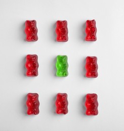 Image of Individuality, uniqueness, different. Green jelly bear among red ones on white background, flat lay