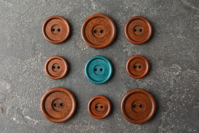 Image of Individuality, uniqueness, different. Turquoise sewing button among brown ones on grey textured background, flat lay