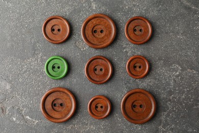 Image of Individuality, uniqueness, different. Green sewing button among brown ones on grey textured background, flat lay