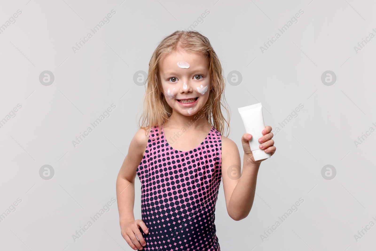 Smiling little girl with tube of sun protection product on grey background Photo of Smiling little girl with tube of sun protection product on grey background