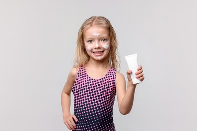 Photo of Smiling little girl with tube of sun protection product on grey background