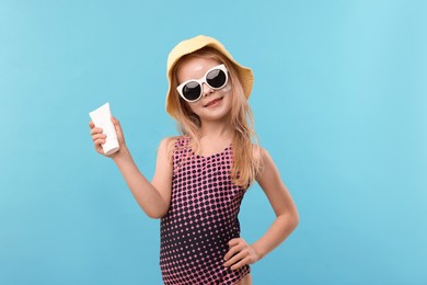 Photo of Cute little girl with tube of sun protection product on light blue background