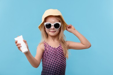 Photo of Cute little girl with tube of sun protection product on light blue background