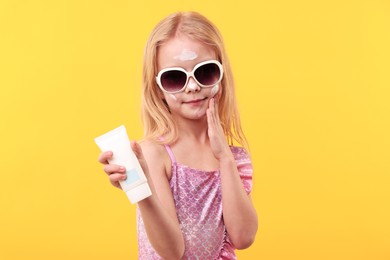 Photo of Cute little girl with tube of sun protection cream against yellow background