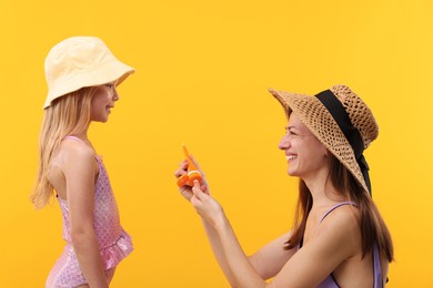 Photo of Smiling mother with tube of sun protection product and her daughter on yellow background