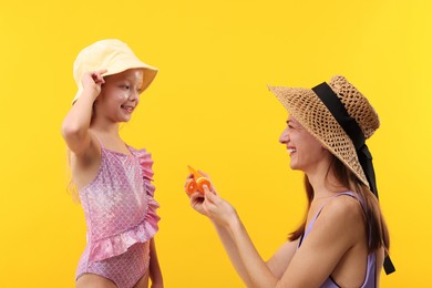 Photo of Smiling mother with tube of sun protection product and her daughter on yellow background