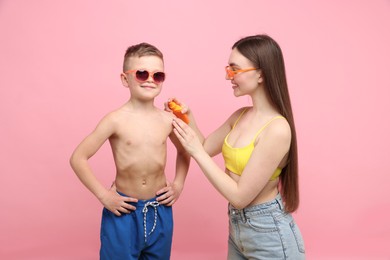 Photo of Mother applying sun protection cream onto her son's skin on pink background