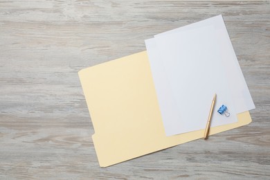 Photo of Paper file folder with blank sheets, pen and binder clip on wooden table, top view. Space for text