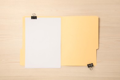 Photo of Paper file folder with blank sheets and binder clips on wooden table, top view
