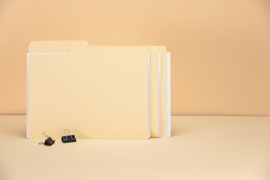 Photo of File folders with papers and binder clips on pale yellow background, space for text
