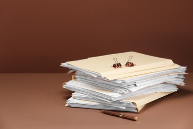 Photo of File folders with papers, pen and binder clips on brown background, space for text