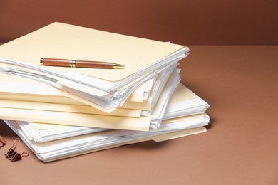 Photo of File folders with papers, pen and binder clip on brown background, closeup