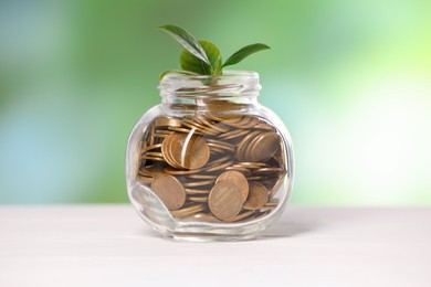 Photo of Investment concept. Glass jar with coins and sprout on light table against blurred green background