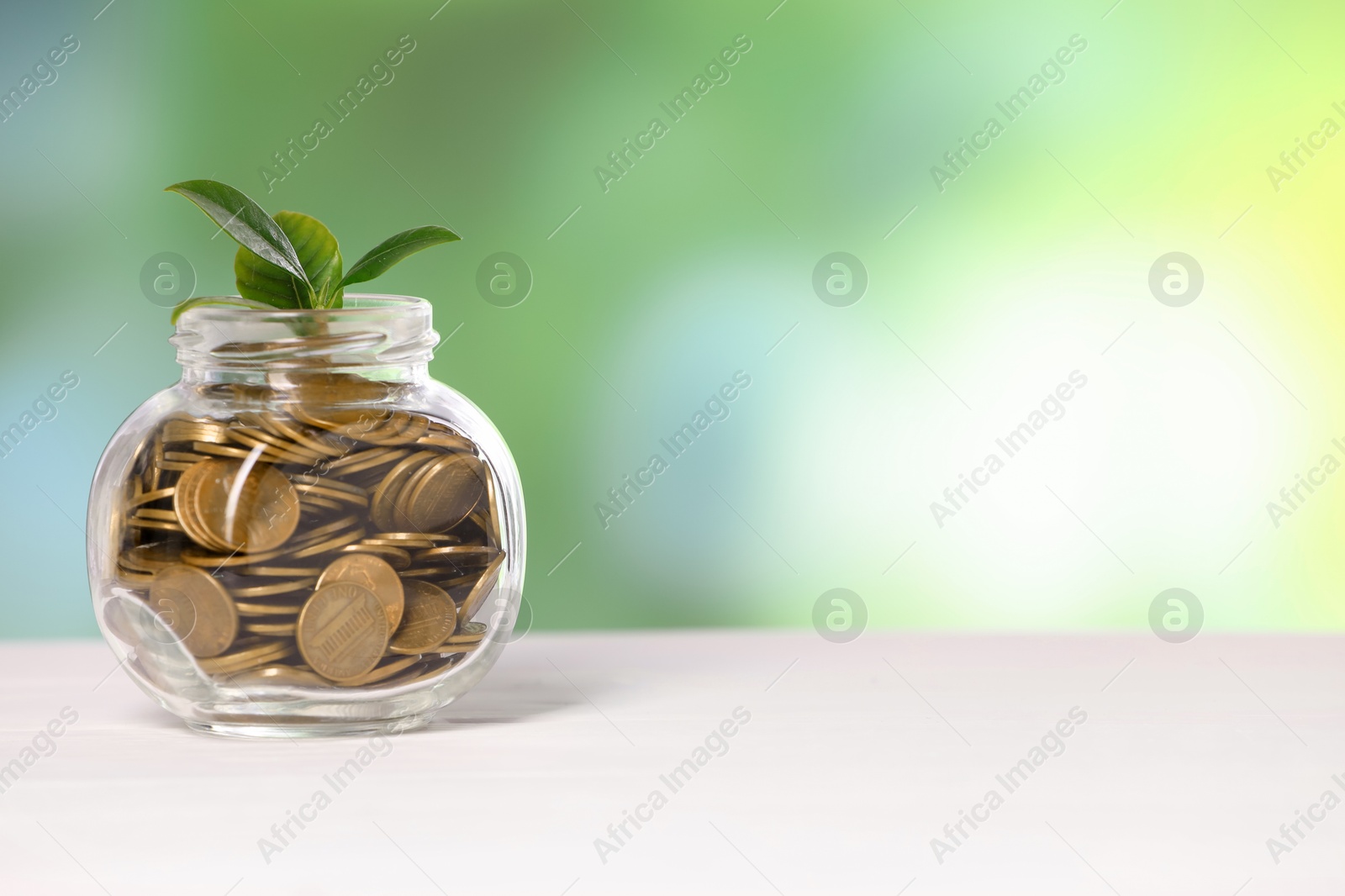 Investment concept. Glass jar with coins and sprout on light table against blurred green background, space for text Photo of Investment concept. Glass jar with coins and sprout on light table against blurred green background, space for text