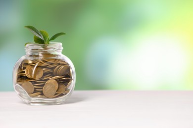 Photo of Investment concept. Glass jar with coins and sprout on light table against blurred green background, space for text