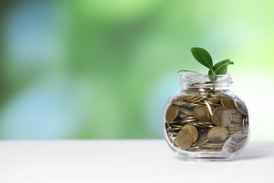 Photo of Investment concept. Glass jar with coins and sprout on light table against blurred green background, space for text