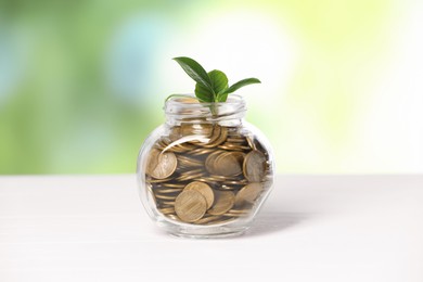 Photo of Investment concept. Glass jar with coins and sprout on light table against blurred green background