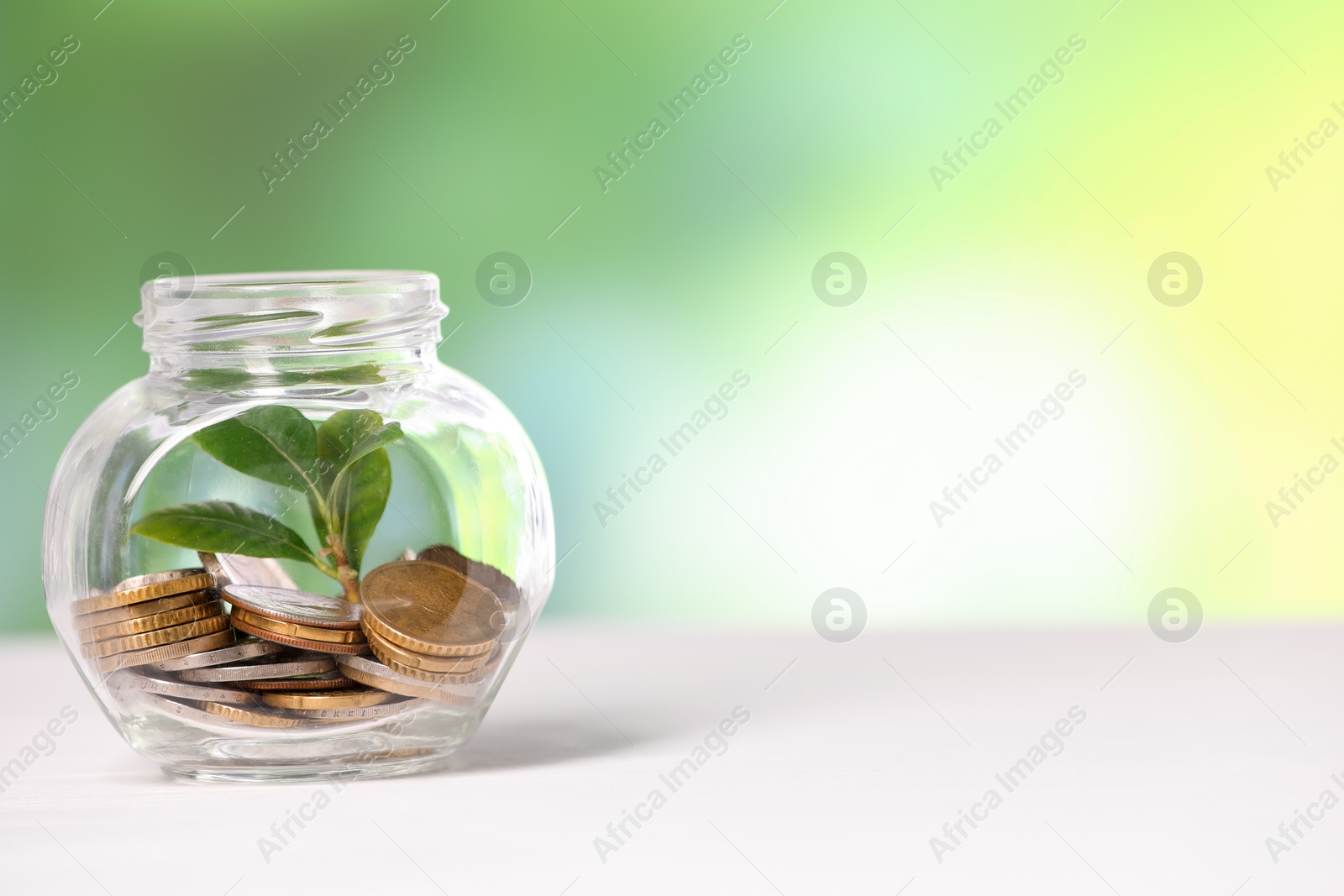 Investment concept. Glass jar with coins and sprout on light table against blurred green background, space for text Photo of Investment concept. Glass jar with coins and sprout on light table against blurred green background, space for text