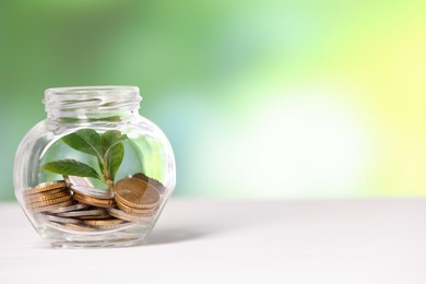 Photo of Investment concept. Glass jar with coins and sprout on light table against blurred green background, space for text