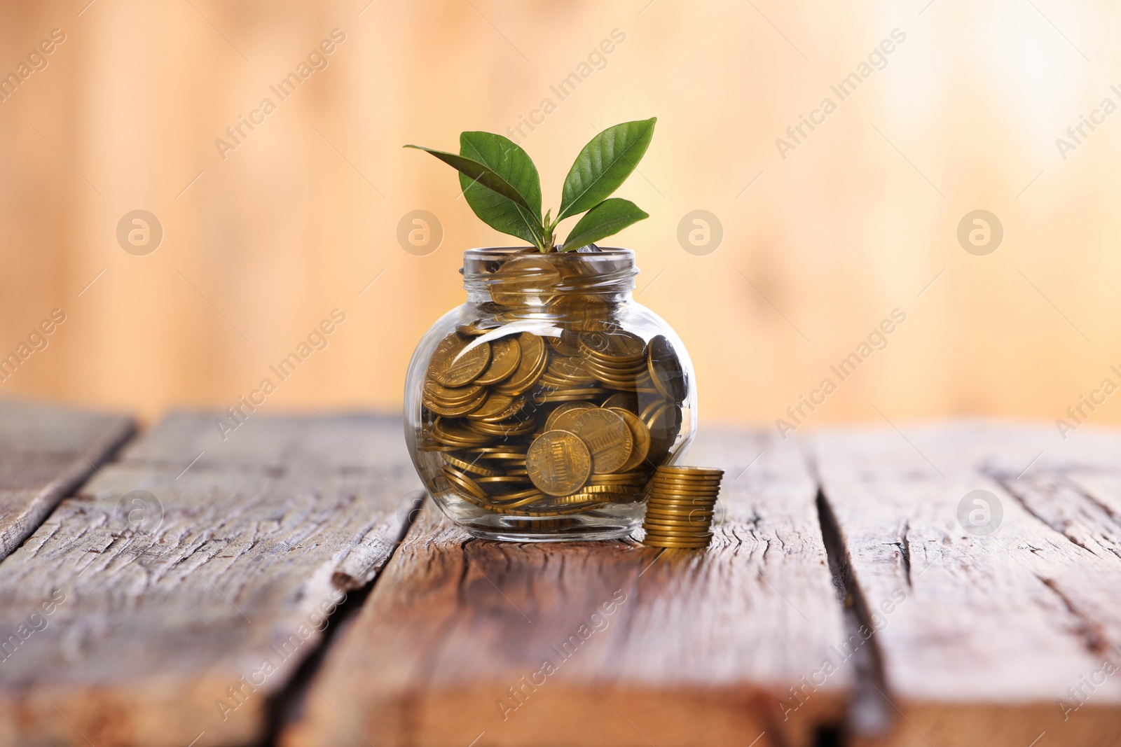 Investment concept. Glass jar with coins and sprout on wooden table against blurred orange background Photo of Investment concept. Glass jar with coins and sprout on wooden table against blurred orange background